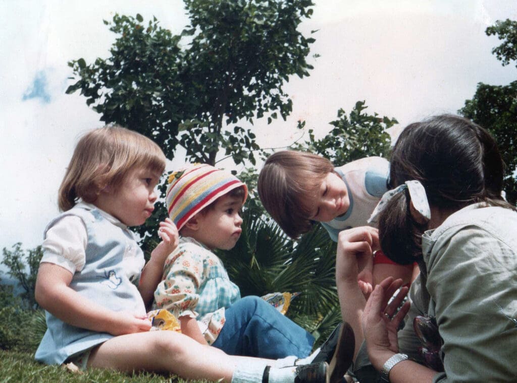 Wendy and her siblings sitting together outdoors during childhood in Venezuela
